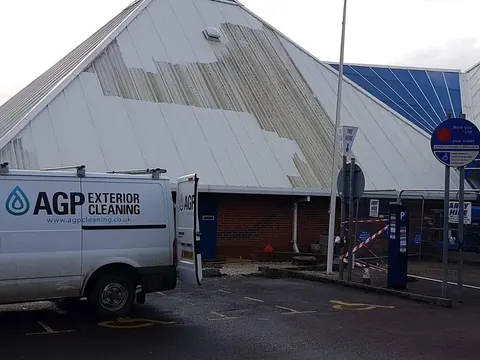 A large commercial pyramid roof half cleaned, with the AGP Exterior Cleaning van parked in front.