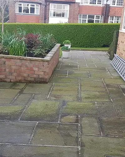 Before: dark, mossy patio flags around a raised brick planter.