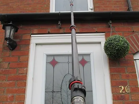 A reach-and-wash pole cleaning an upstairs window of a brick house.